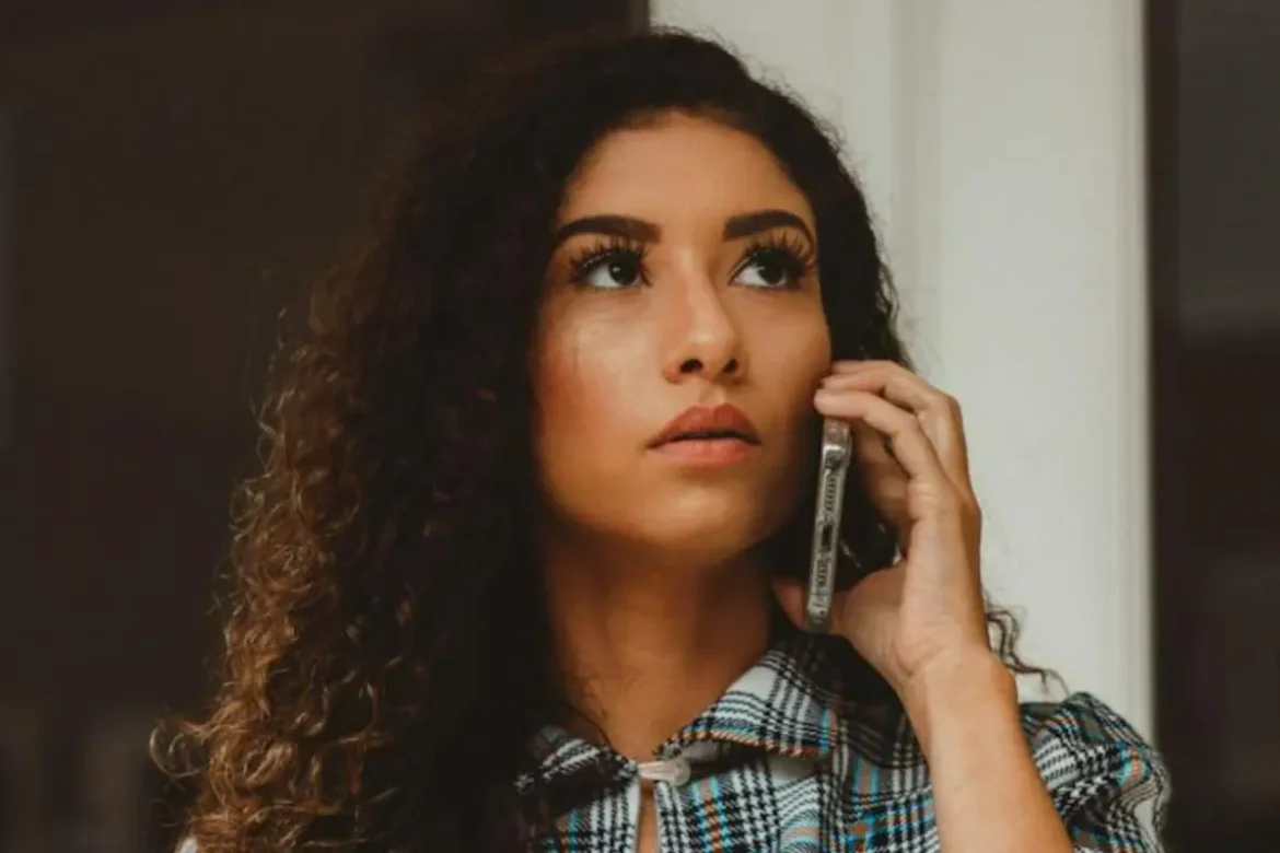 Woman with long curly hair with a hesitant face expression talking on her cellphone.