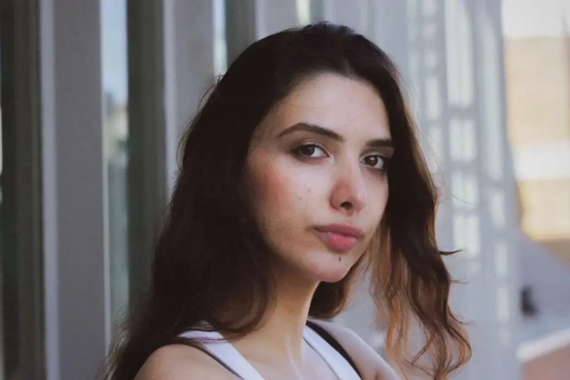 Woman standing outside looking at camera wearing a serious expression.