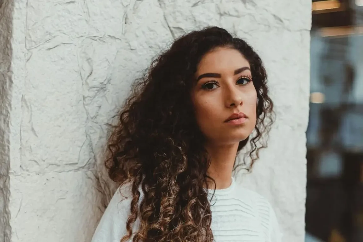 Woman outside standing against wall looking into camera with a defeated face expression.