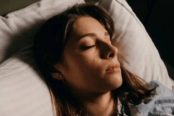 Woman laying in bed with eyes closed and a flushed face expression.
