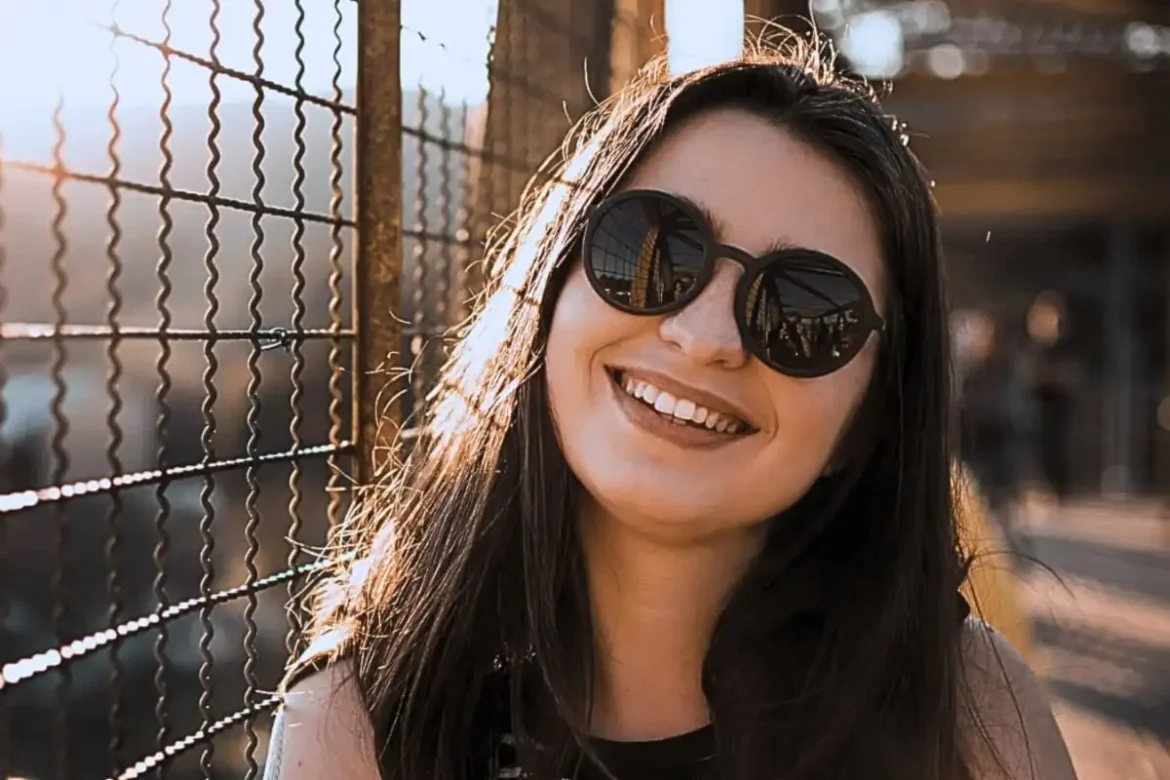 A woman outdoors wearing sunglasses smiling into the camera.