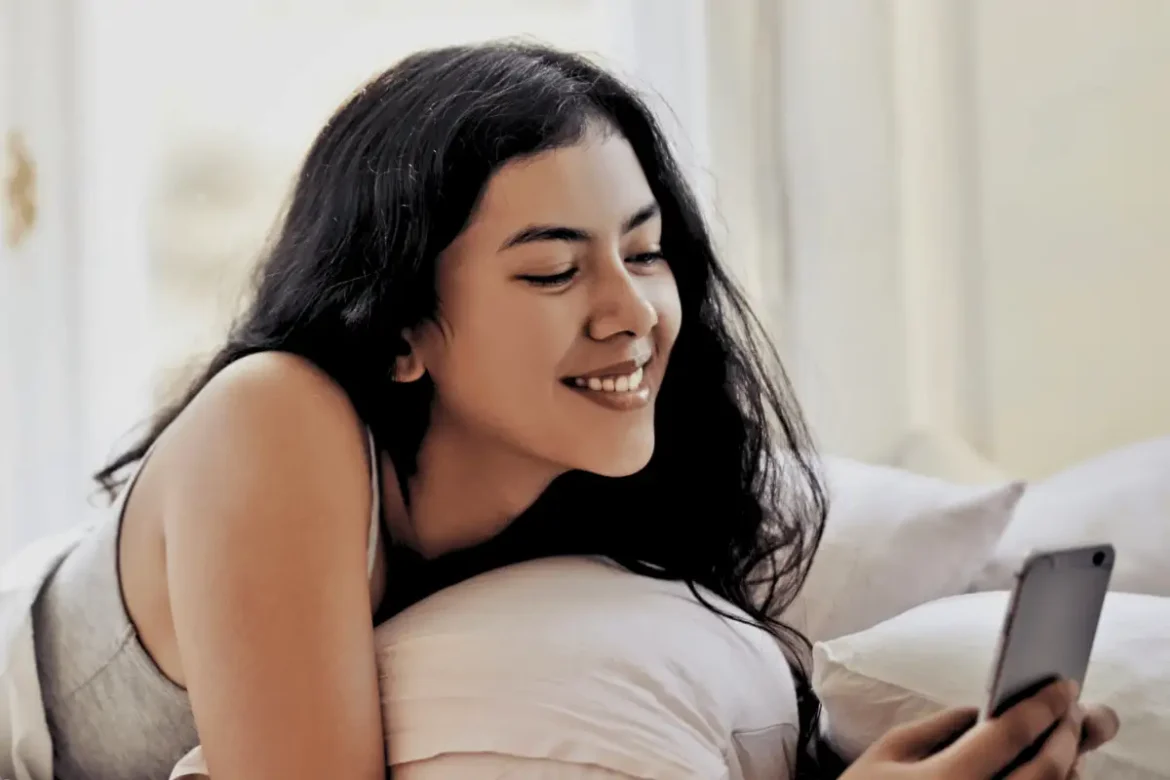 Young woman laying on bed texting on her cellphone with a smug face expression