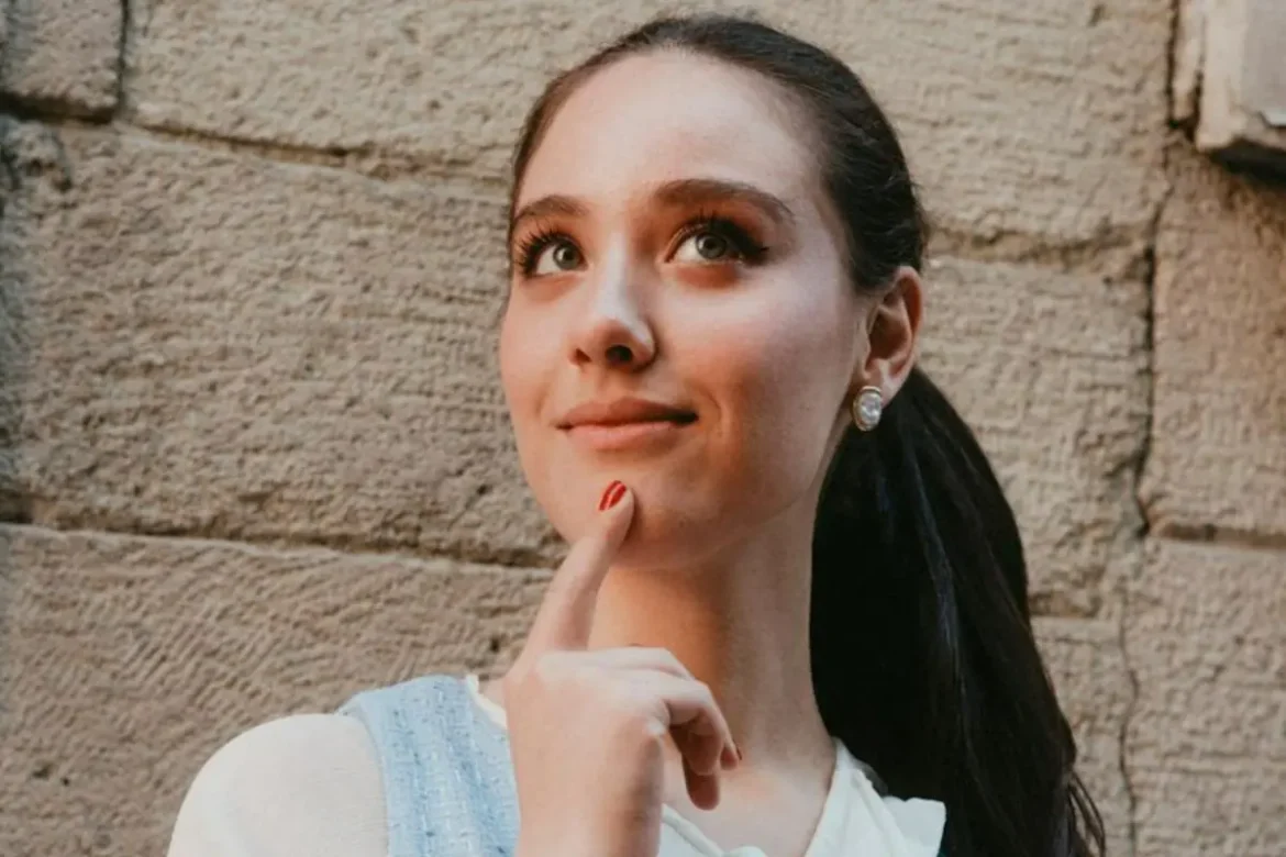Young woman with a ponytail touching her chin with one finger, wearing a thoughtful expression.
