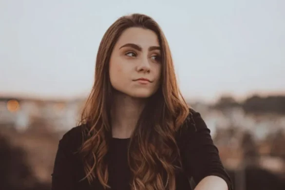 Young woman with long brown hair outdoors, looking deep in thought.