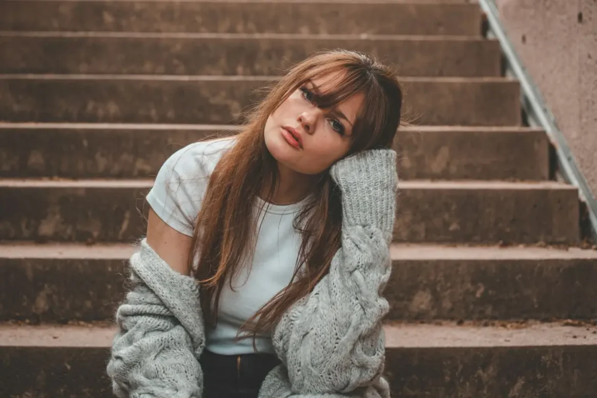 Young woman outside sitting on steps with a hand resting on the side of her face.