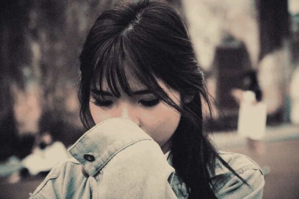 A woman covering her face with a sad face expression.