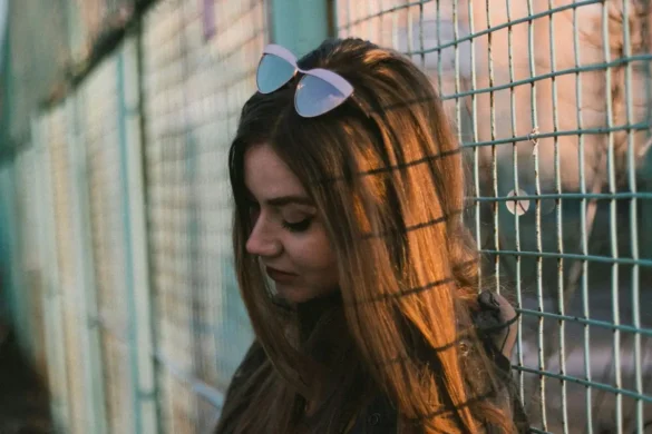 Woman standing against chain fence with a sad expression.